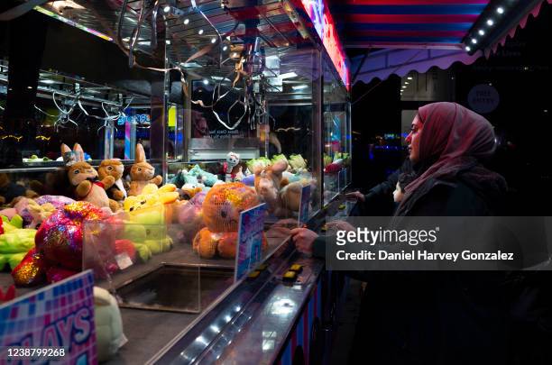 Young woman wearing a headscarf looks attentively at the claw of the teddy picker she is playing on at the fun fair on 25th February, 2022 in Leeds,...