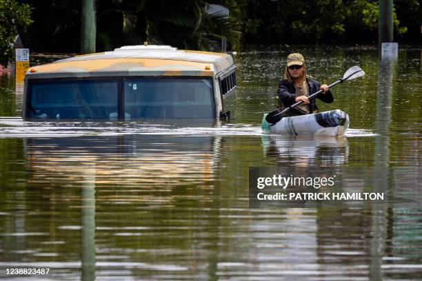 Man paddles his kayak next to a submerged bus on a flooded street in the town of Milton in suburban Brisbane on February 28, 2022.