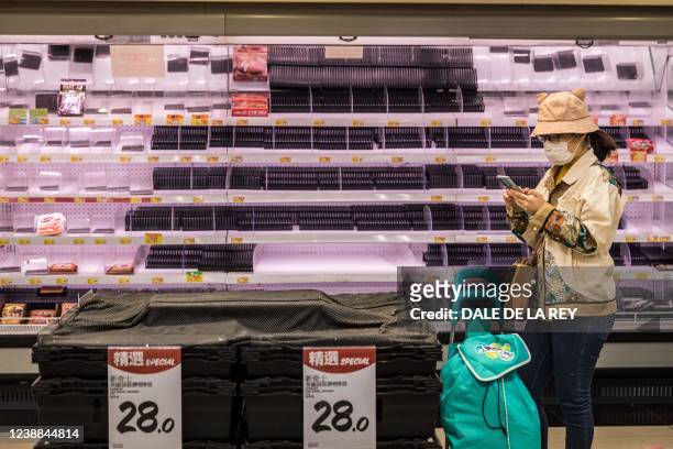 Woman looks at her phone in front of empty shelves at a supermarket in Hong Kong on March 1 as panic buying returned to the city this week with many...
