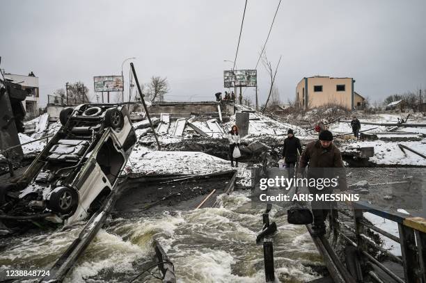 Civilians cross a river on a blown up bridge on Kyivs northern front on March 1, 2022. - Defending capital Kyiv, the "key priority" Ukrainian...