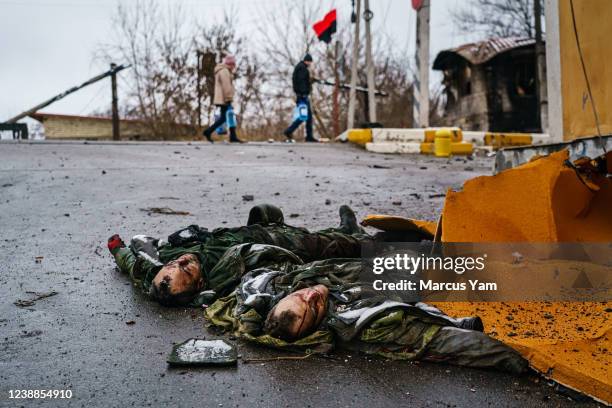 Residents carrying water supply walk briskly past the bodies of dead Russian soldiers, where Ukrainian soldiers fought and repealed Russian forces on...