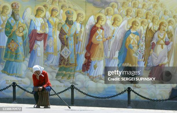 Old woman dozes as she asks for alms in front of frescos of Mikhaylo Gold Cupolas cathedral in Kiev during a hot summer day in Ukraine's capital 06...