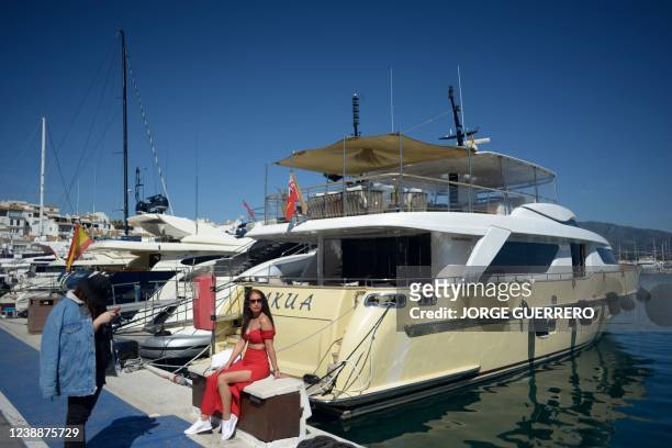 Woman sits next to a yacht in Puerto Banus luxury marina and shopping complex in Marbella on March 2, 2022. - Marbella is one of the favorite...
