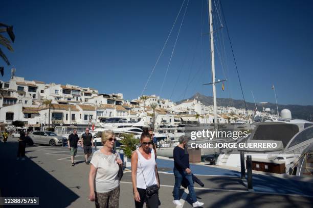 People stroll in Puerto Banus luxury marina and shopping complex in Marbella on March 2, 2022. - Marbella is one of the favorite destinations for...