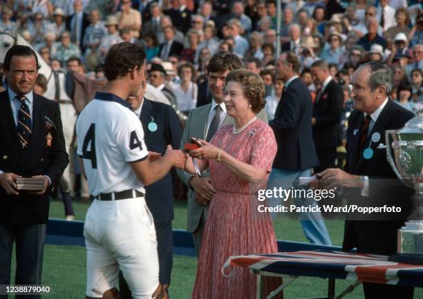 Queen Elizabeth II presenting a medal to her son Charles, The Prince of Wales, following a polo match at Cowdray Park near Midhurst, circa August...