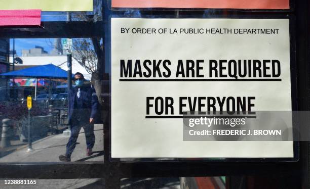 Man wearing a protective face mask walks past a sign requiring face masks posted on a storefront in Los Angeles, California, on March 2, 2022. - Los...