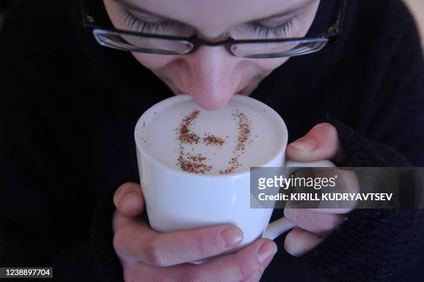 Coffeehouse client holds a cup of cappuccino with the portrait of Vladimir Putin created with cinnamon and cocoa powder sprinkled on the cappuccino's...