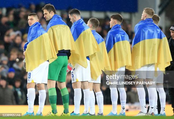 Everton's Ukrainian defender Vitaliy Mykolenko and teammates stand draped in national flags of Ukraine ahead of the English FA Cup fifth round...