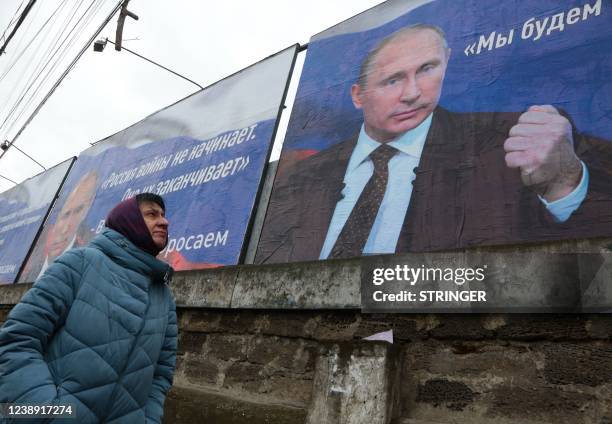 Woman walks past huge placards bearing images of Russian President Vladimir Putin and reading "Russia does not start wars, it ends them" and "We will...