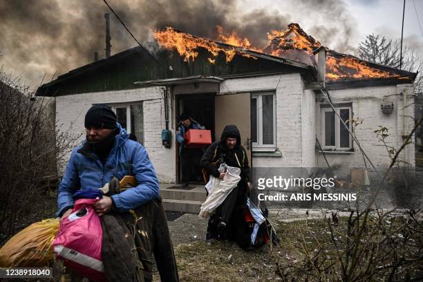 People remove personal belongings from a burning house after being shelled in the city of Irpin, outside Kyiv, on March 4, 2022. - More than 1.2...