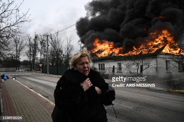 Woman reacts as she stands in front of a house burning after being shelled in the city of Irpin, outside Kyiv, on March 4, 2022. - More than 1.2...