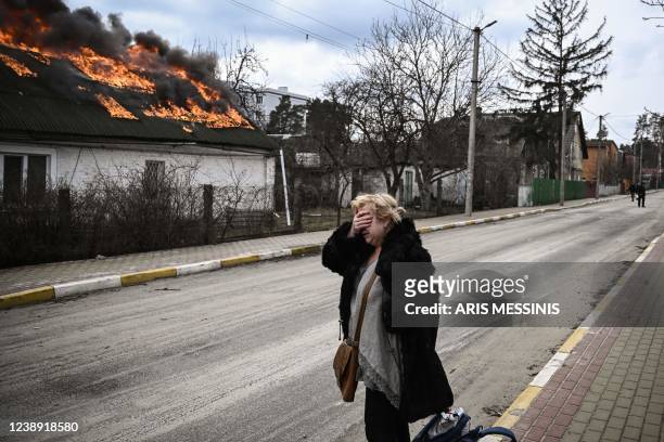 Woman reacts as she stands in front of a house burning after being shelled in the city of Irpin, outside Kyiv, on March 4, 2022. - More than 1.2...