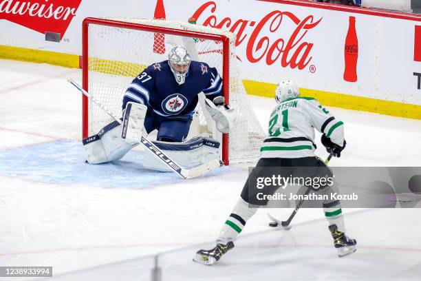 Jason Robertson of the Dallas Stars plays the puck towards goaltender Connor Hellebuyck of the Winnipeg Jets during first period action at the Canada...