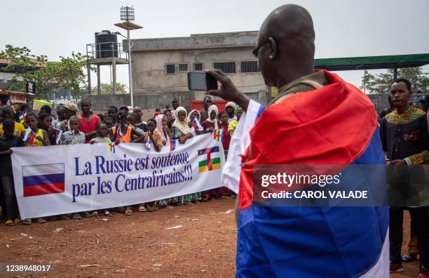 Man draped in a Russian flag takes pictures of demonstrators gathering in Bangui on March 5, 2022 during a rally in support of Russia. - A hundred...