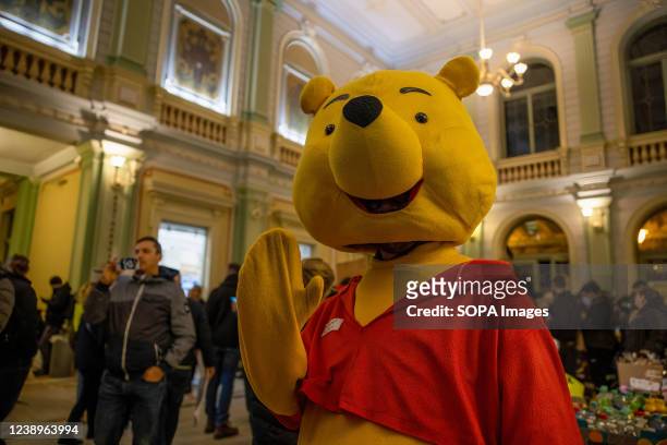 Volunteer is dressing up in Winnie the Pooh costume to entertain young refugees at the train station. Hundreds of thousands of refugees from Ukraine...