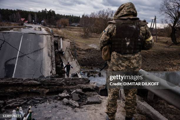 An Ukrainian serviceman looks at a civilian crossing a blown up bridge in a village, east of the town of Brovary on March 6, 2022. - The Russian push...