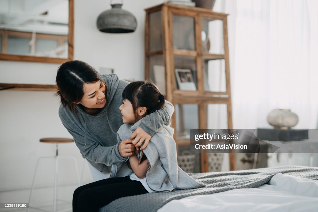 Caring young Asian mother putting a coat on her daughter at home
