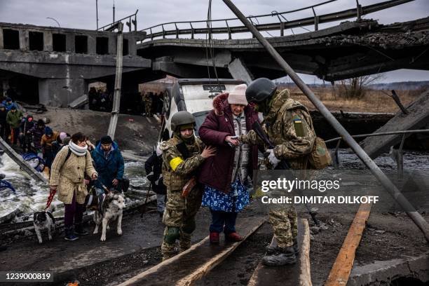 Ukrainian soldiers help an elderly woman to cross a destroyed bridge as she evacuates the city of Irpin, northwest of Kyiv, on March 7, 2022. -...