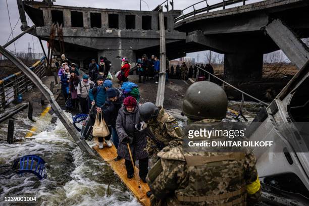 Evacuees cross a destroyed bridge as they flee the city of Irpin, northwest of Kyiv, on March 7, 2022. - Ukraine dismissed Moscow's offer to set up...