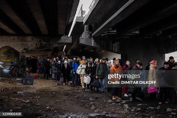 Evacuees stand under a destroyed bridge as they flee the city of Irpin, northwest of Kyiv, on March 7, 2022. - Ukraine dismissed Moscow's offer to...