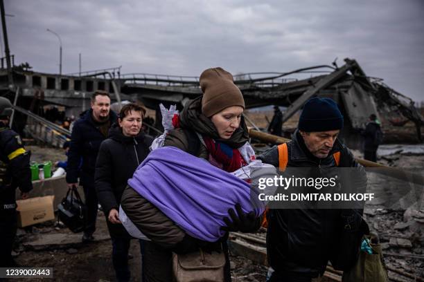 Woman carrying her baby crosses a destroyed bridge as they flee the city of Irpin, northwest of Kyiv, on March 7, 2022. - Ukraine dismissed Moscow's...