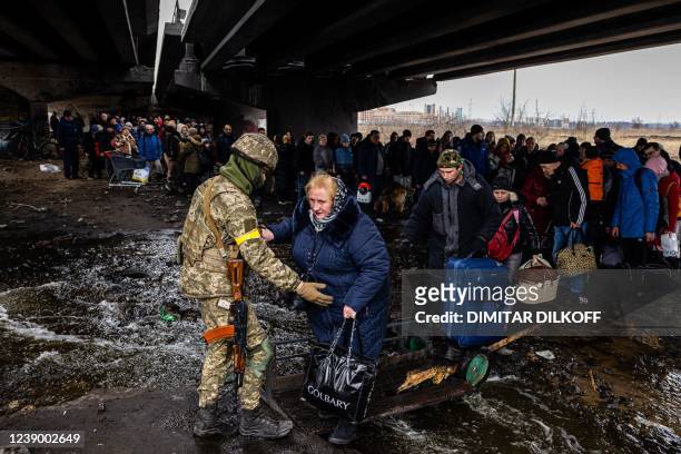Ukrainian serviceman helps evacuees gathered under a destroyed bridge, as they flee the city of Irpin, northwest of Kyiv, on March 7, 2022. - Ukraine...