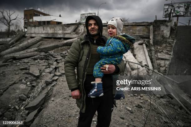 Man holds a child as he flees the city of Irpin, west of Kyiv, on March 7, 2022. - Russian forces pummelled Ukrainian cities from the air, land and...