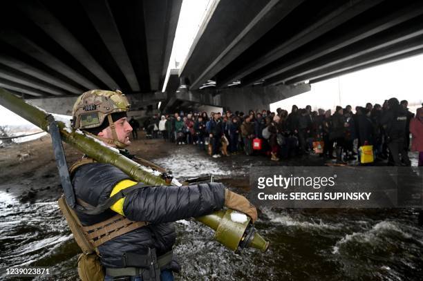 Ukrainian serviceman holding a sa-16 gimlet Man-portable air-defense system looks at people crossing a destroyed bridge during the evacuation by...