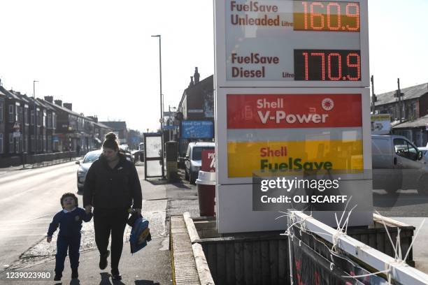 People walk past a board indicating the prices of petrol and diesel fuel at a Shell petrol station, in Manchester, on March 8, 2022. - Energy giant...
