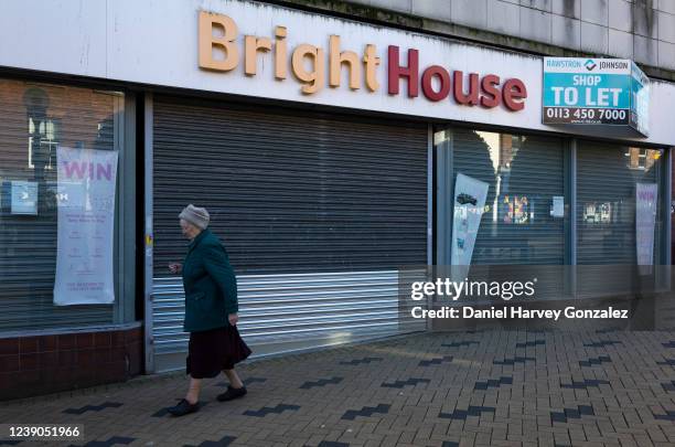 An elderly woman walks past a permanently closed branch of the former high street pay weekly chain BrightHouse that is now advertised as being "to...