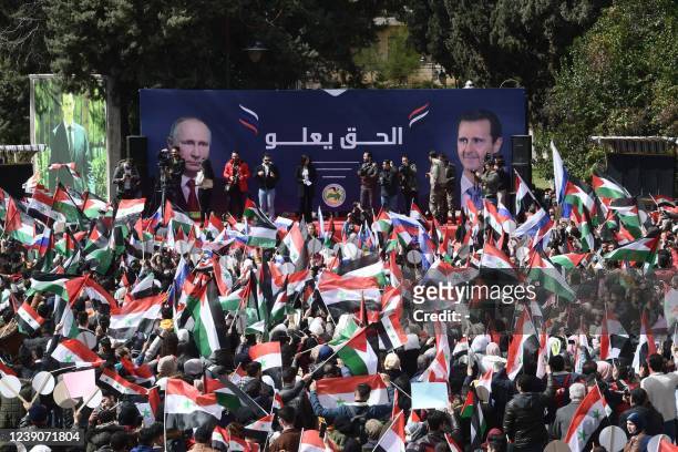 Syrian students wave the Syrian, Russian and Palestinian flags under a billboard bearing the portraits of Syrian President Bashar al-Assad and...