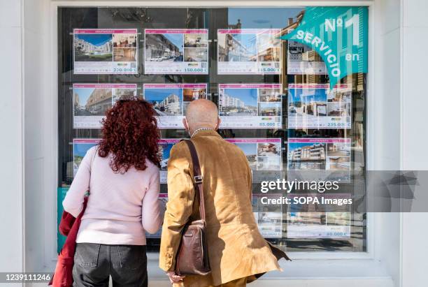 Couple looks for housing offerings for sale and rents at a real estate property agent in Spain.