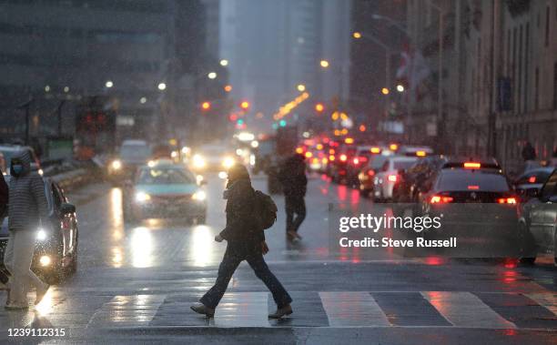 Pedestrian crosses Front Street at Bay Street as snow falls in the downtown area in Toronto. March 11, 2022.