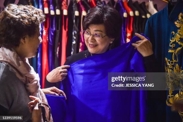 This photo taken on December 2, 2021 shows a customer trying on a piece of fabric for her custom-made Qipao with a tailor at a Qipao studio in...