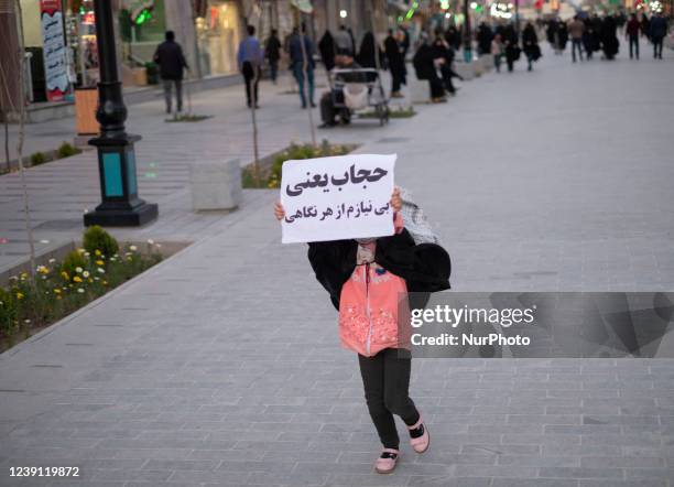 An Iranian young girl demonstrates a placard with a Persian script that said, Hijab means I do not need any look, while walking along a street near a...