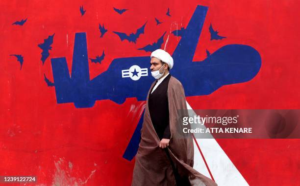An Iranian cleric walks past an anti-US mural on a wall of the former United States embassy in the capital Tehran, on March 12, 2022. - Iran said...