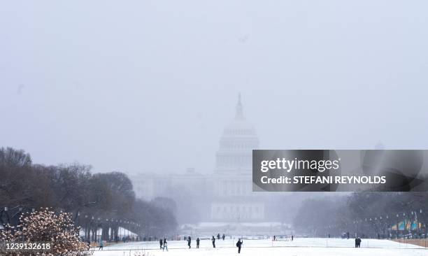 The US Capitol is seen past visitors along the National Mall in Washington, DC, on March 12, 2022. - Winter storm warnings and winter weather...