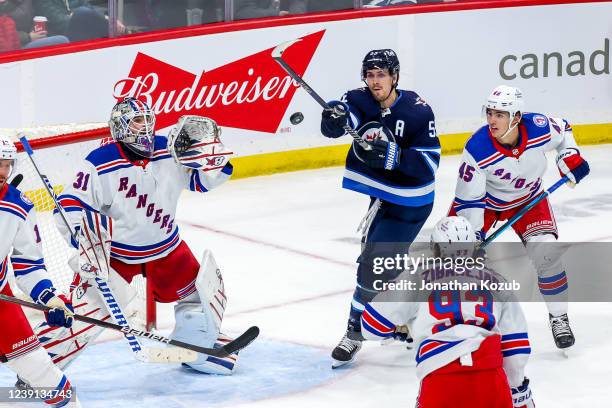 Mark Scheifele of the Winnipeg Jets swipes at the flying puck while goaltender Igor Shesterkin, Mika Zibanejad, and Braden Schneider of the New York...