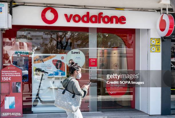 Pedestrian uses a smartphone as she walks past British multinational telecommunications corporation and phone operator, Vodafone, store in Spain.