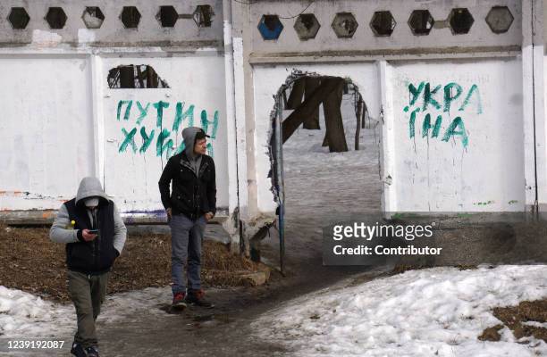 Man looks at graffiti on a fence which reads "Putin is a fucker" and "Ukraine", on March 14, 2022 in Moscow, Russia. Anti-war and anti-Putin graffiti...