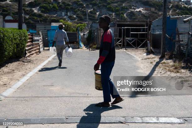 People walk with buckets while looking for a tap with running water in Zwelitsha, an informal settlement in Khayelitsha that is home to millions of...