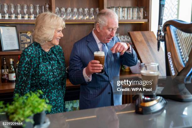 Prince Charles, Prince of Wales holds a pint of Guinness he has poured as he stands next to Camilla, Duchess of Cornwall during a visit to The Irish...