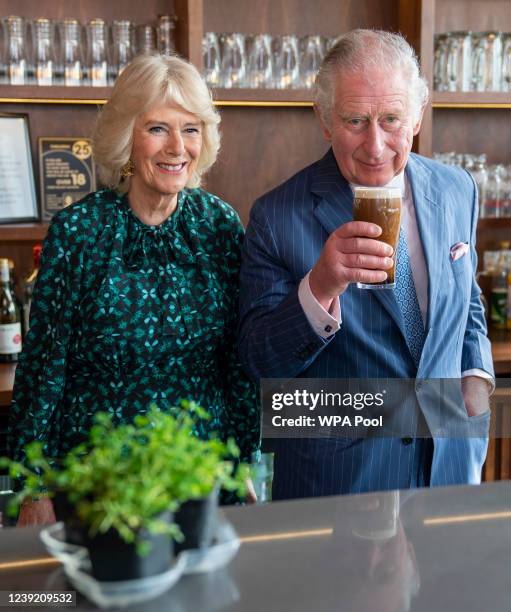 Prince Charles, Prince of Wales holds a pint of Guinness he has poured as he stands next to Camilla, Duchess of Cornwall during a visit to The Irish...