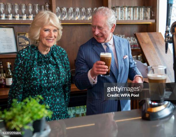 Prince Charles, Prince of Wales holds a pint of Guinness he has poured as he stands next to Camilla, Duchess of Cornwall during a visit to The Irish...