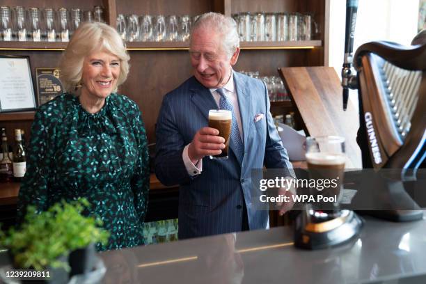 Prince Charles, Prince of Wales holds a pint of Guinness he has poured as he stands next to Camilla, Duchess of Cornwall during a visit to The Irish...