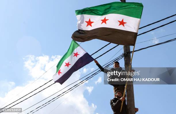 Syrians stand on an electric pole as they wave opposition flags during a rally marking 11 years since the start of an anti-regime uprising in Syria's...