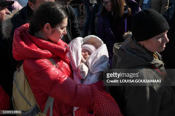 Woman holds her baby wrapped in pink as people stand waiting to board buses for their further transportation after crossing from Ukraine into Poland...