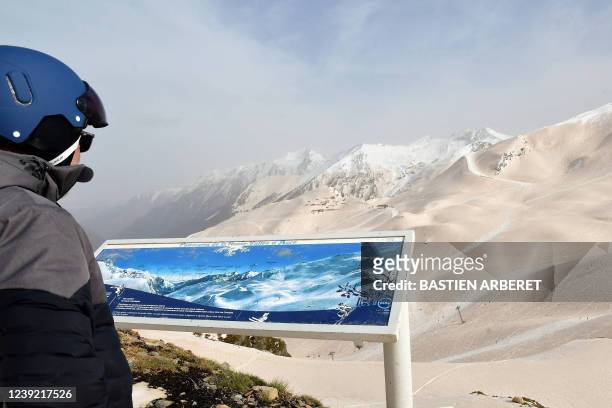 Skier looks on as sand from Sahara felt overnight covering the snow, in Piau-Engaly ski ressort, southwestern France, on March 15, 2022. - Orange...