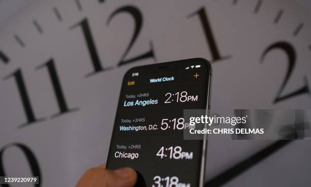 This illustration photo shows a clock in the background of a smartphone showing the time after daylight saving time was implemented in Los Angeles,...