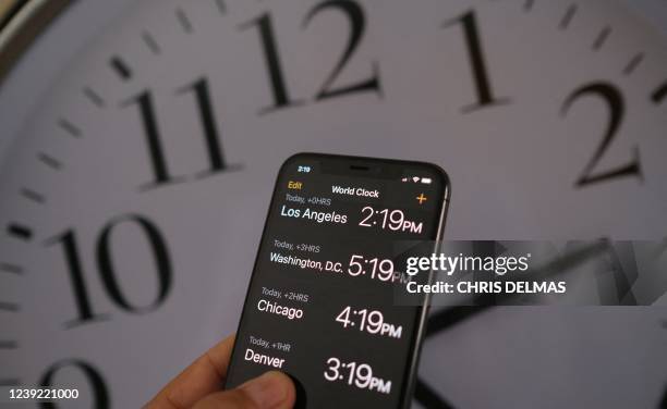 This illustration photo shows a clock in the background of a smartphone showing the time after daylight saving time was implemented in Los Angeles,...